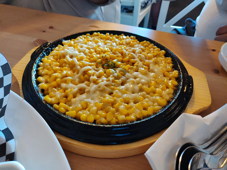 Corn covered in melted cheese served in a sizzling pan.