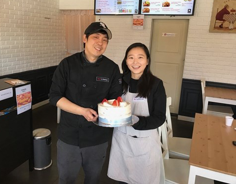 Sean Kim and his wife Jiyoo in uniform holding a cake.